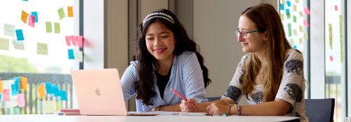 Two students working on a project together using sticky notes and laptops